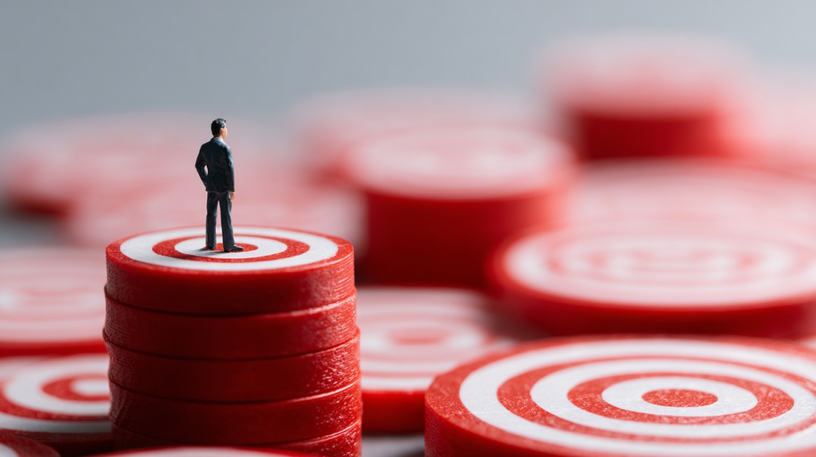 Tiny figurine of a person in a suit standing on stacked red target discs with more targets blurred in the background